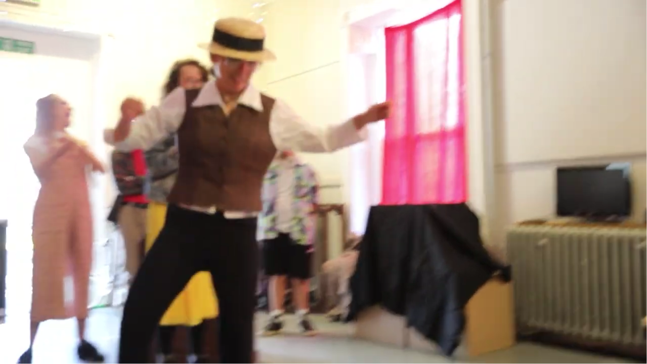 A blurry action shot of Chrissie, in a boater hat an waistcoat leaping in the air.