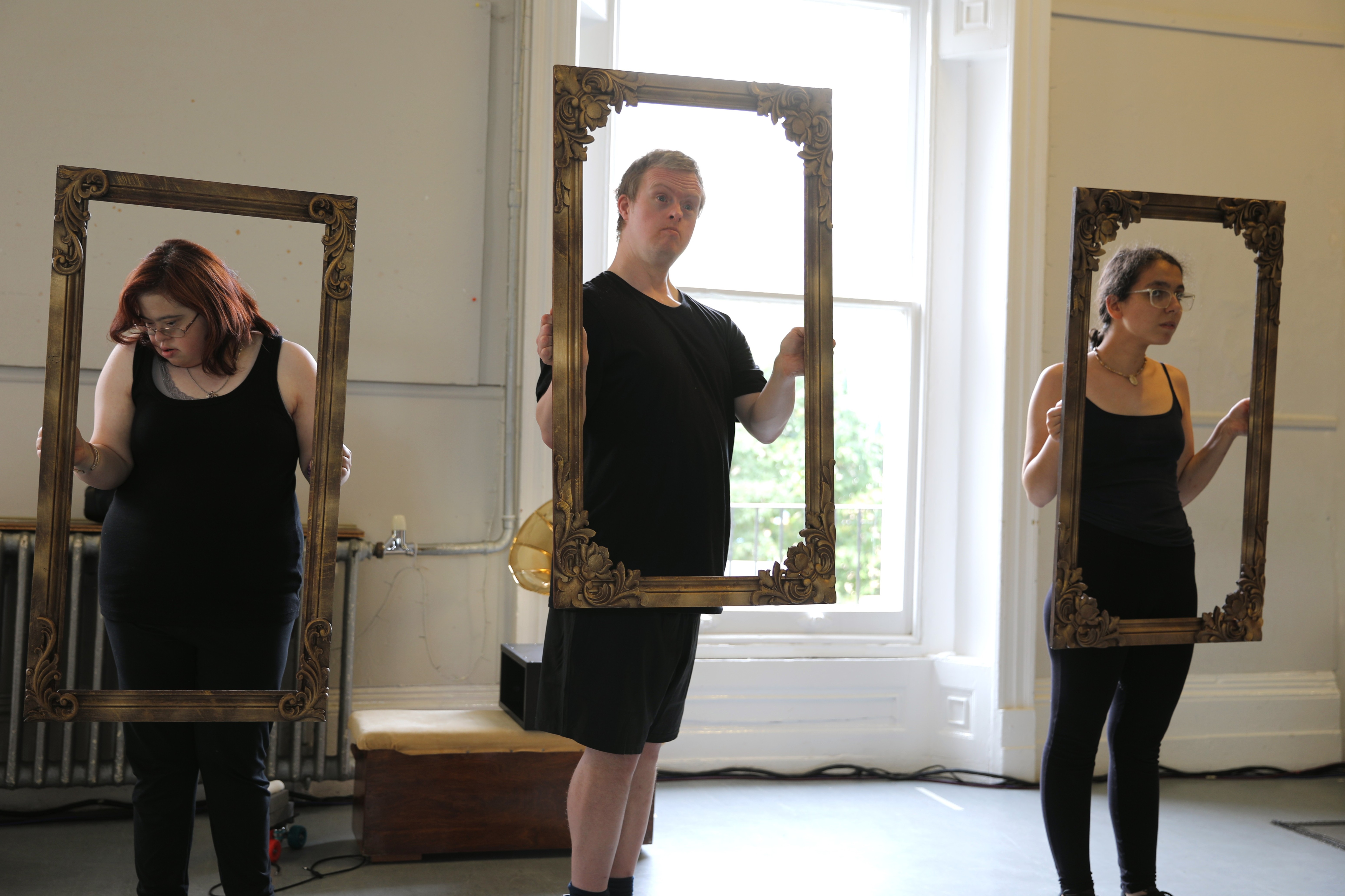 Three performers, wearing black, are each holding a picture frame. They pose as if they are the painted figures.