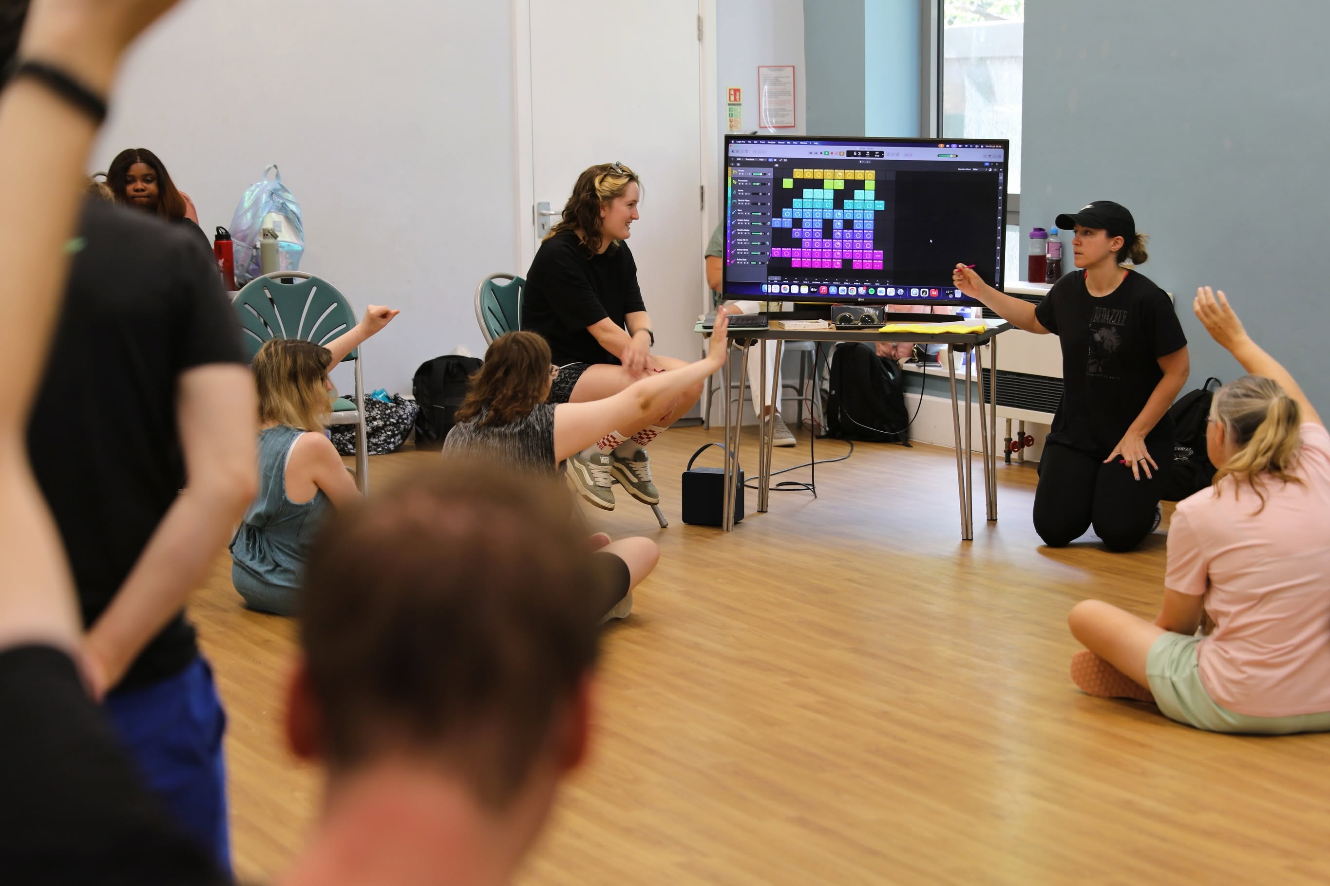 A Bedazzle group takes part in a creative workshop, with participants seated in a circle while a facilitator leads the activity beside a large screen.